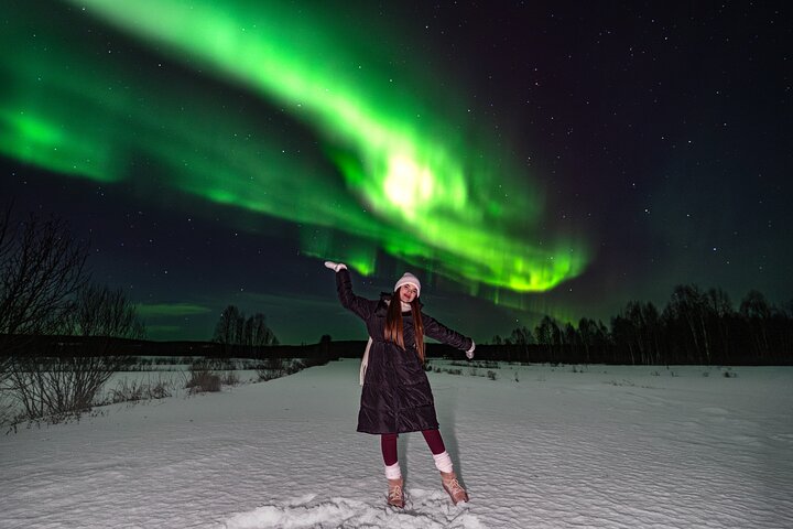 Guest with arms raised in the snow beneath green aurora