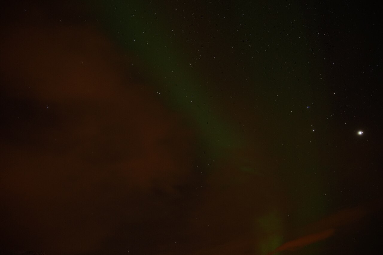 A faint aurora near Tromsø: pale green bands in a dark, hazy sky