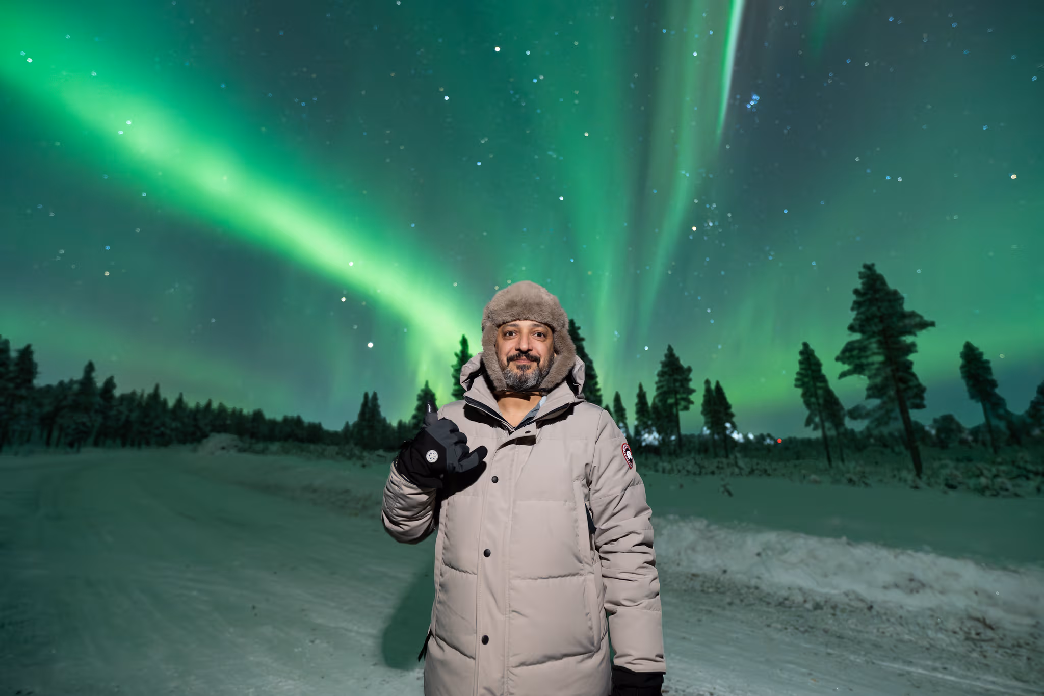 Guest in a pale coat waving beneath green aurora