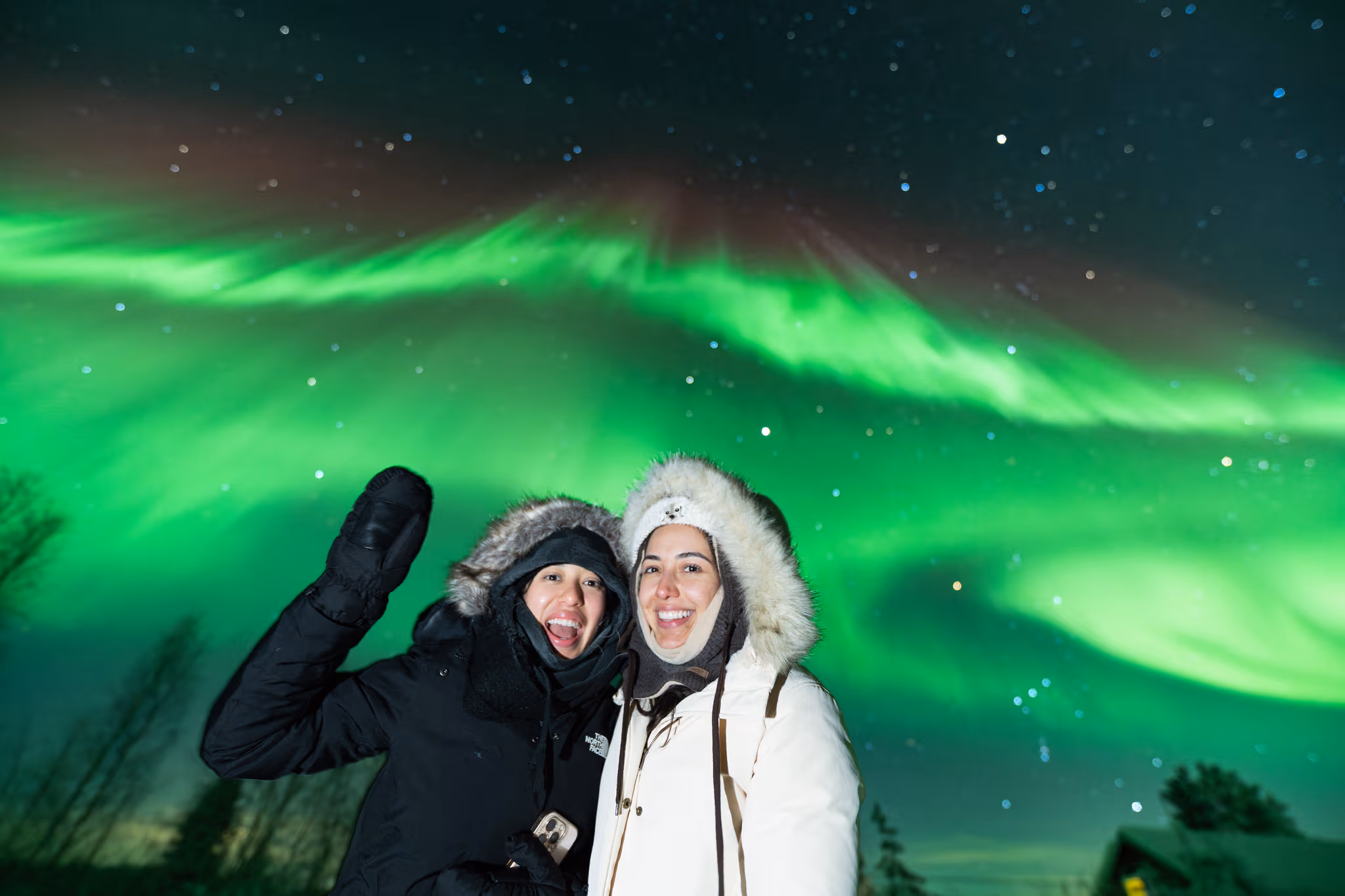 Two guests smiling beneath green aurora