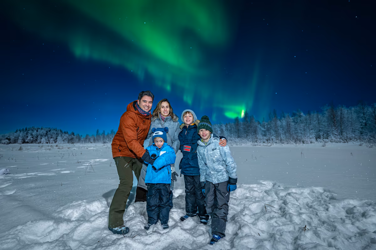Family around a campfire in the Lapland wilderness at night with aurora overhead