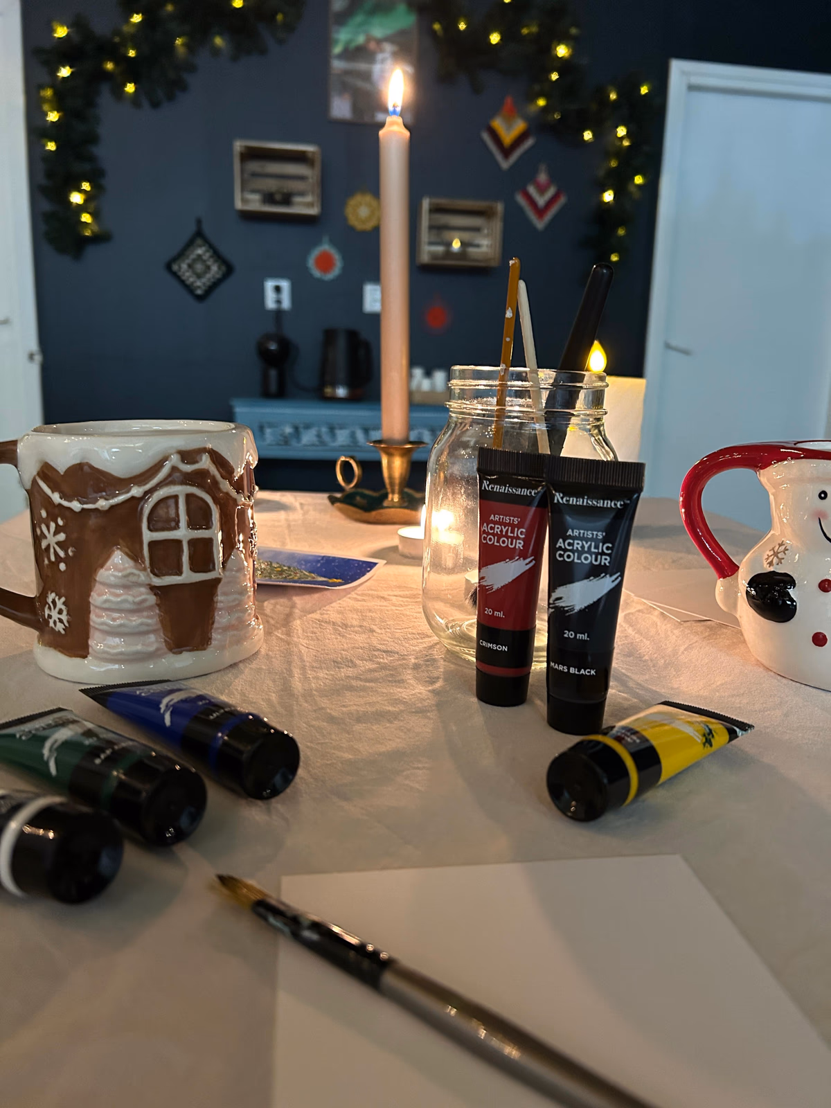 Paints, brushes and festive mugs on the postcard workshop table